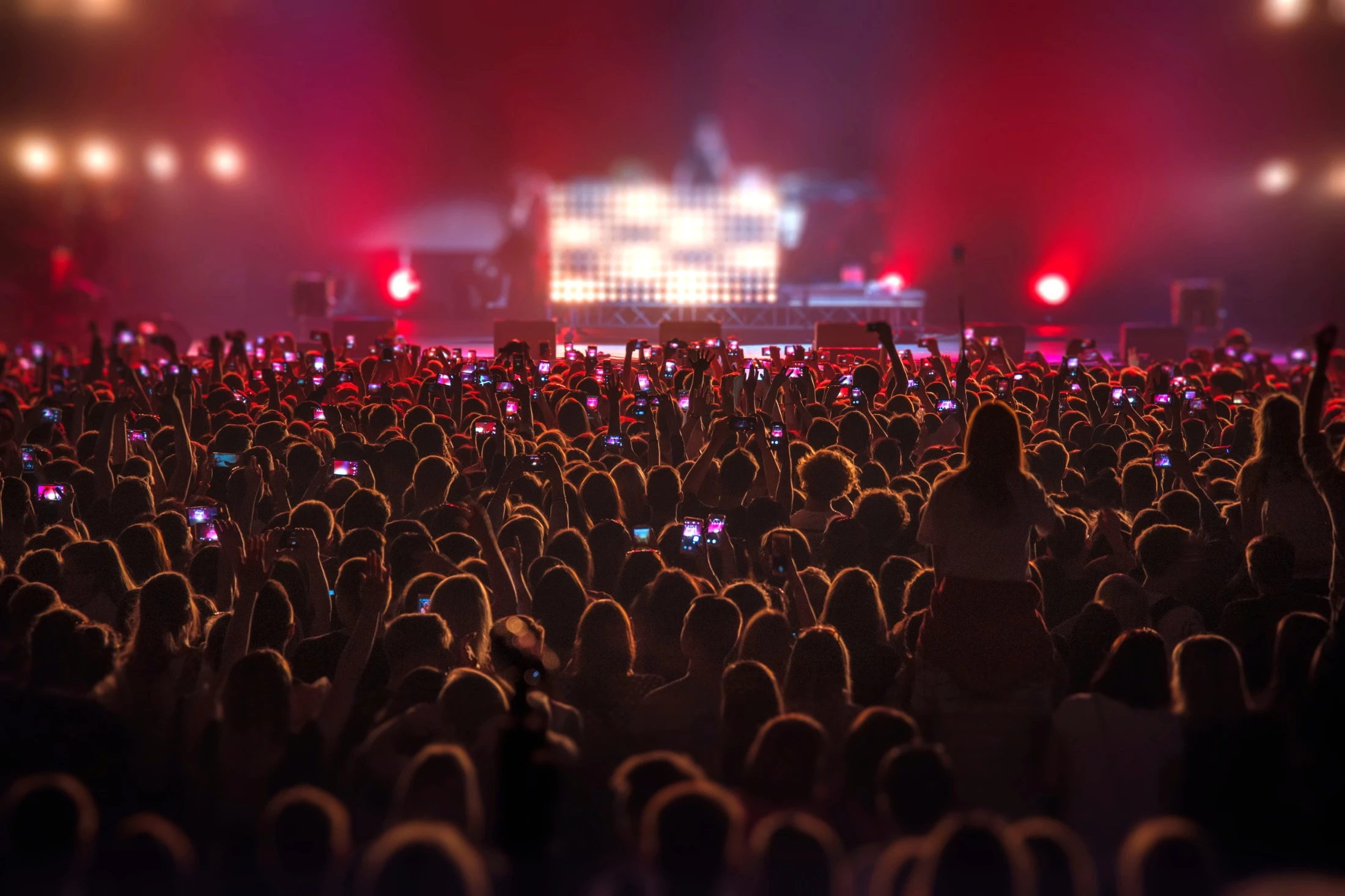 A crowd of people with their hands in the air or filming with their phones at a concert.