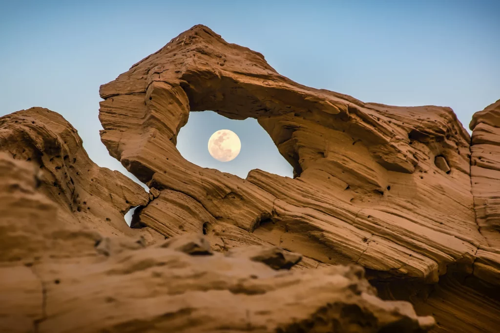 The moon seen through a gap in one of Al Wathba Fossil Dunes.