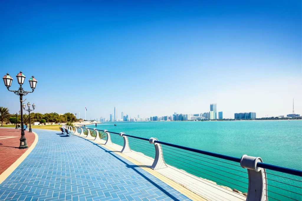 Panoramic view of Abu Dhabi's Corniche with azure waters leading looking towards a skyline of skyscrapers.