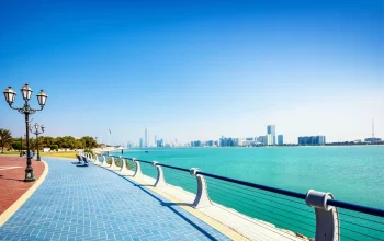 Panoramic view of Abu Dhabi's Corniche with azure waters leading looking towards a skyline of skyscrapers.