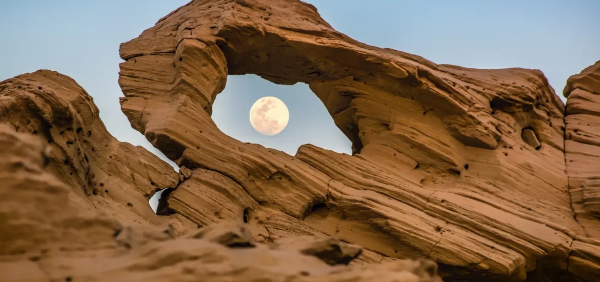 The moon seen through a gap in one of Al Wathba Fossil Dunes.