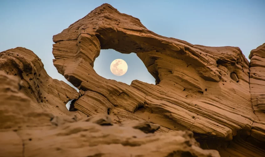 The moon seen through a gap in one of Al Wathba Fossil Dunes.