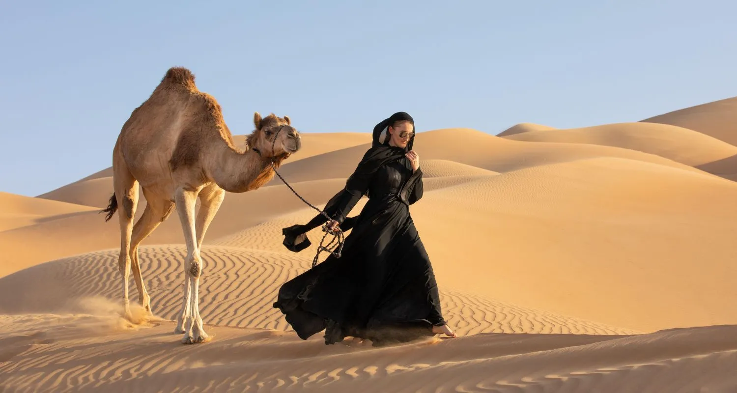 Woman walking with a camel across golden dunes during desert safari in Abu Dhabi