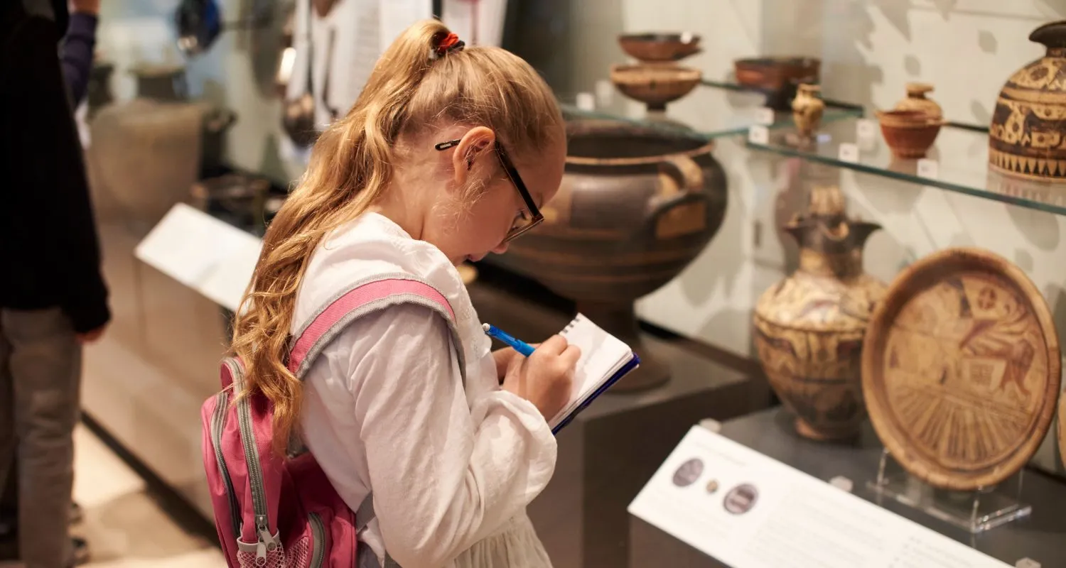 Child learning inside a museum gallery with ancient artifacts and display cases