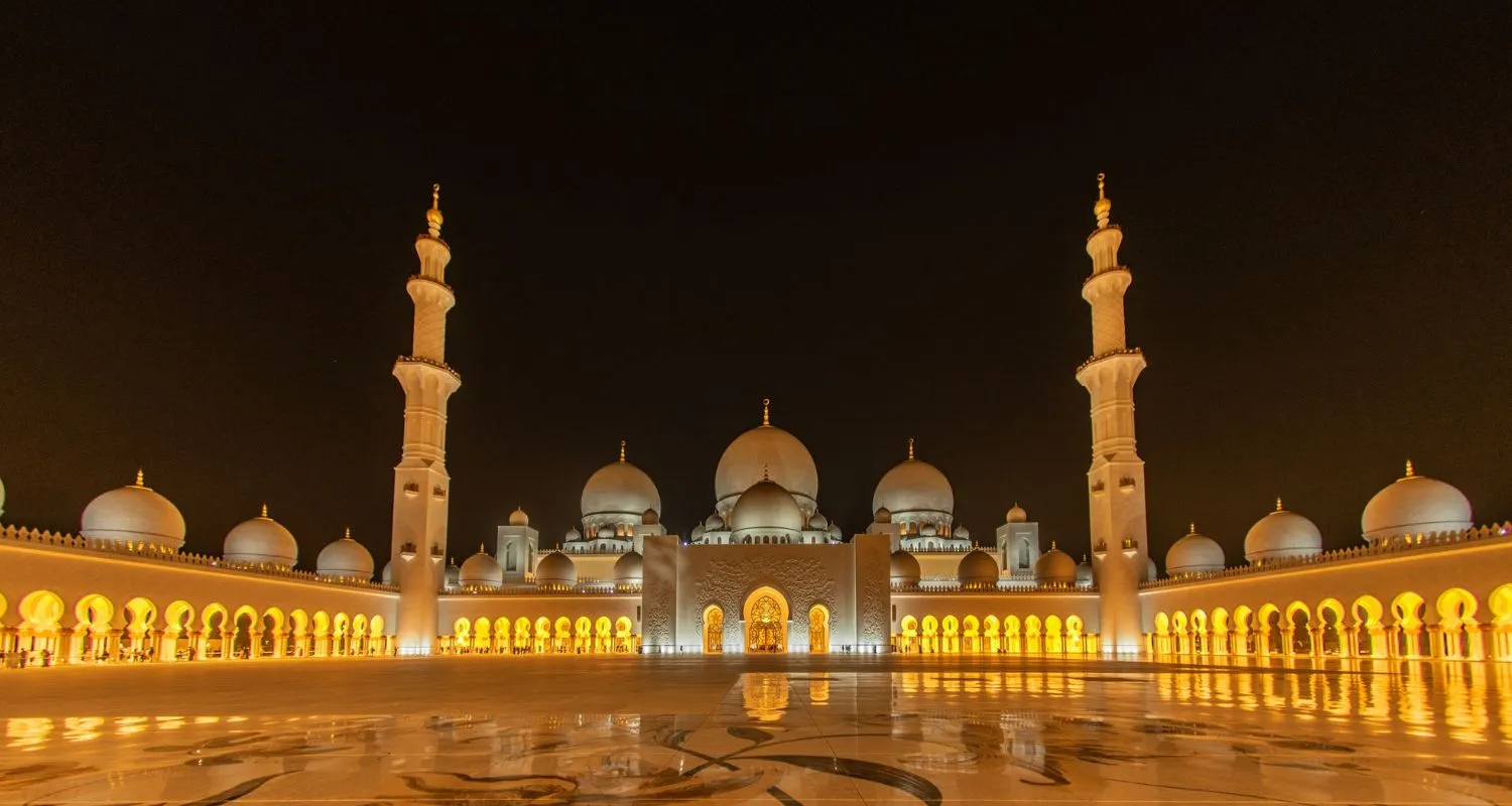 Sheikh Zayed Grand Mosque illuminated at night with golden reflections across the courtyard