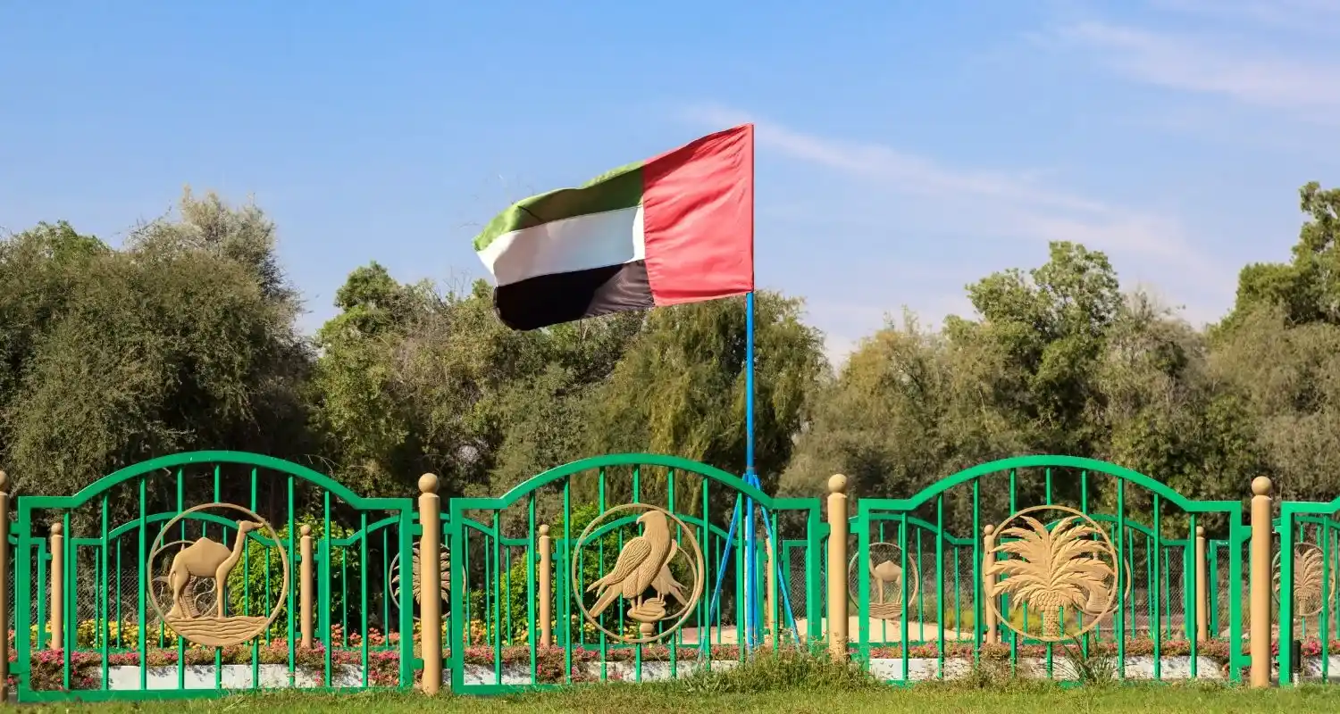 Emirati heritage fence in Liwa Oasis with camel, falcon, and date palm emblems beneath the UAE flag