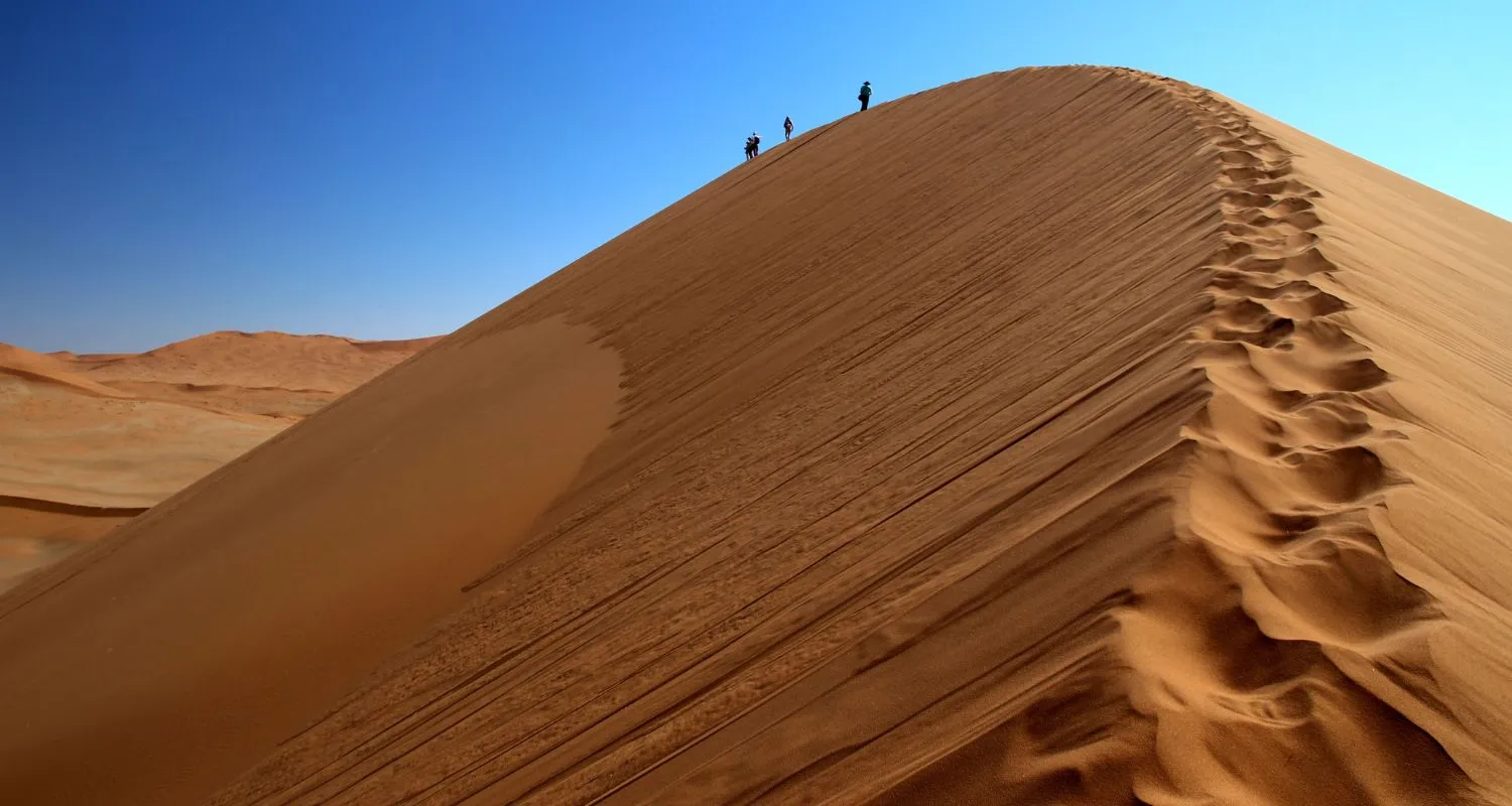 Hikers climbing a towering red sand dune in Abu Dhabi's Empty Quarter