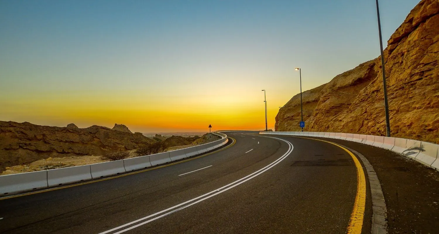 Curving Jebel Hafeet mountain road at sunset with golden cliffs and empty tarmac