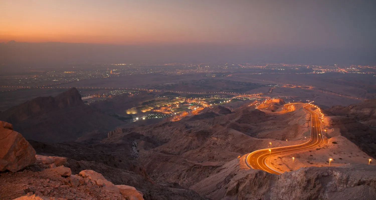 One of the top things to do in Al Ain, the winding Jebel Hafeet road glowing at dusk above the city lights